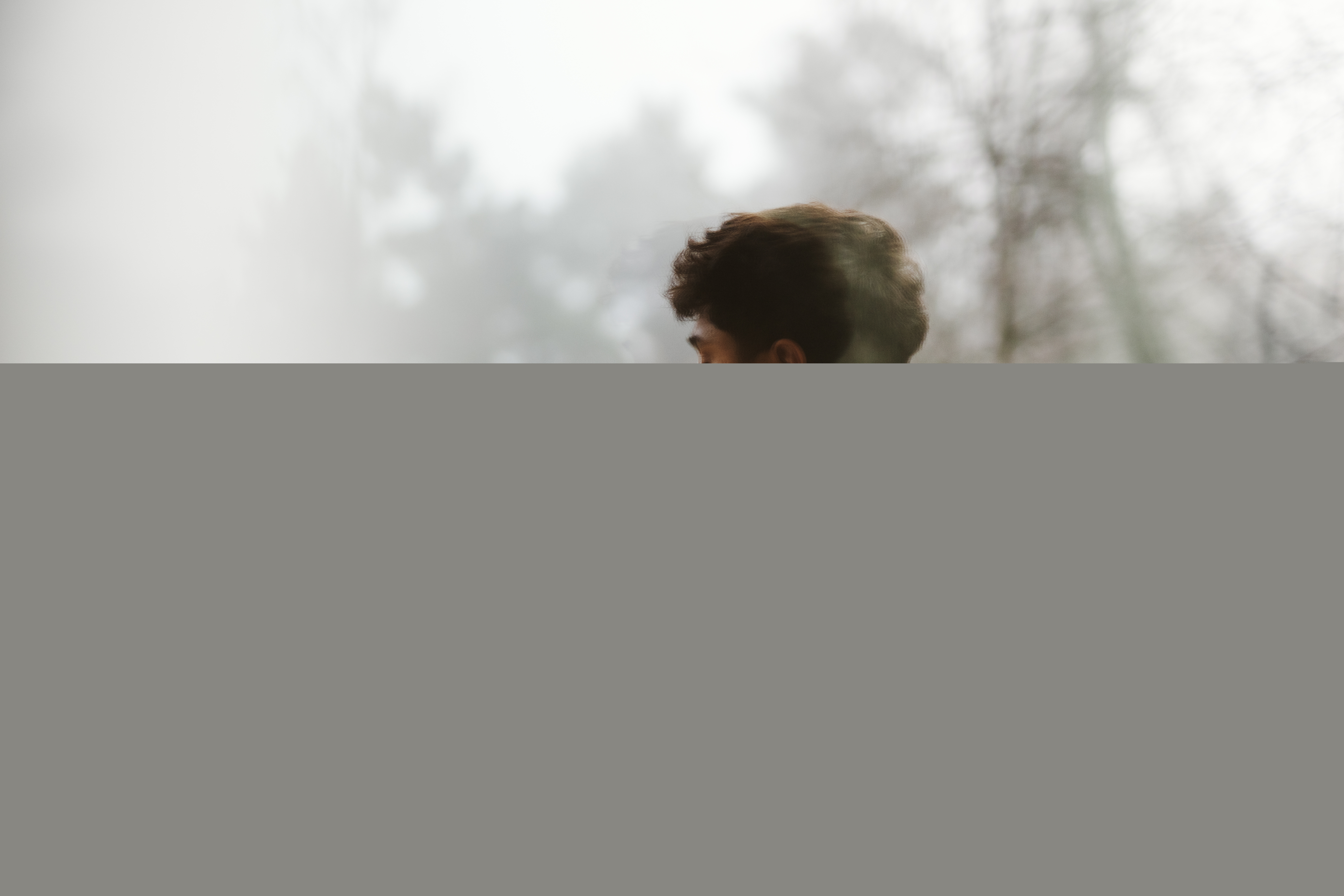 En ung man utomhus. Träd och dimma i omgivningen.