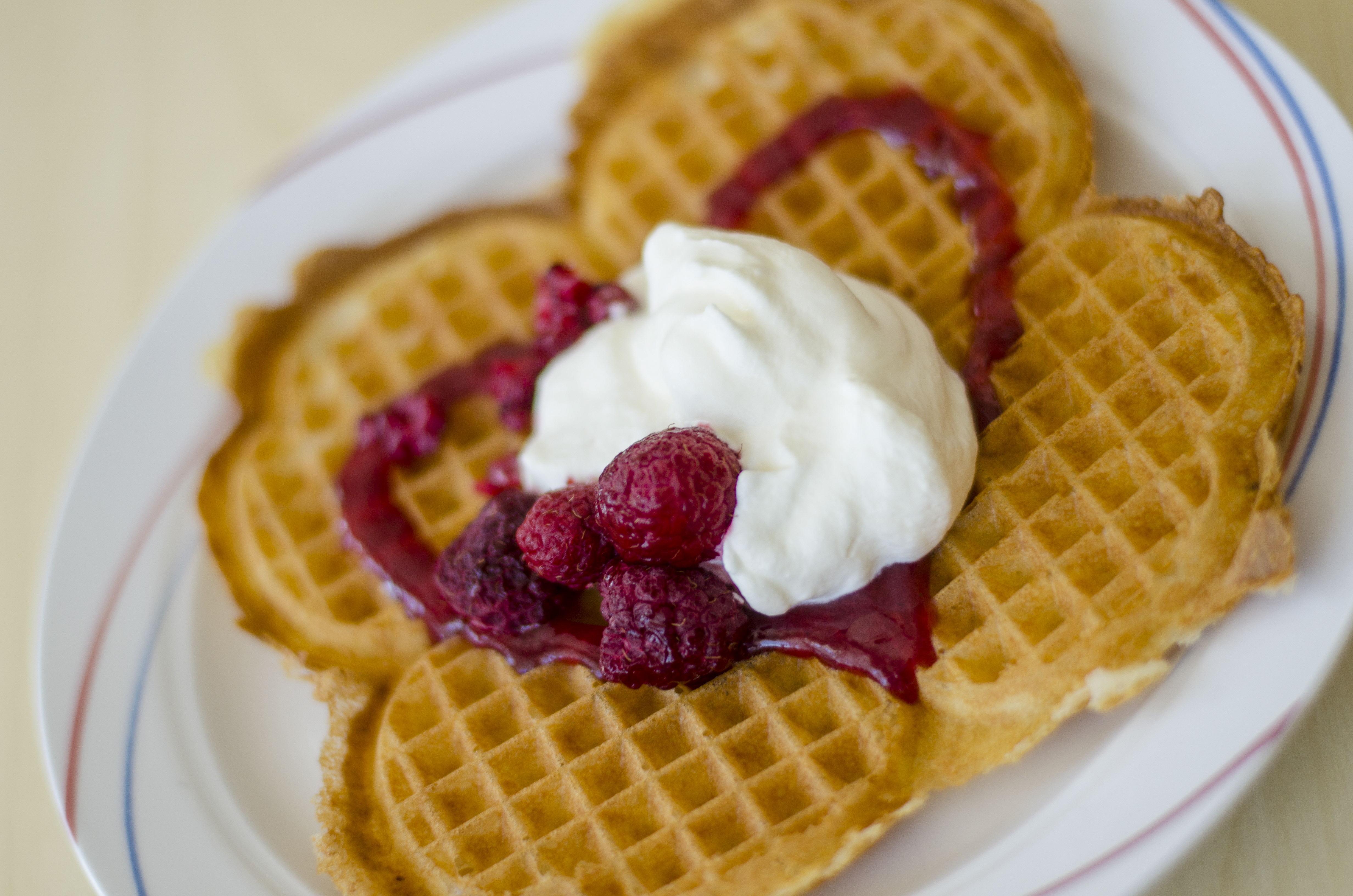 Närbild på en tallrik med en våffla med grädde och hallonsylt.