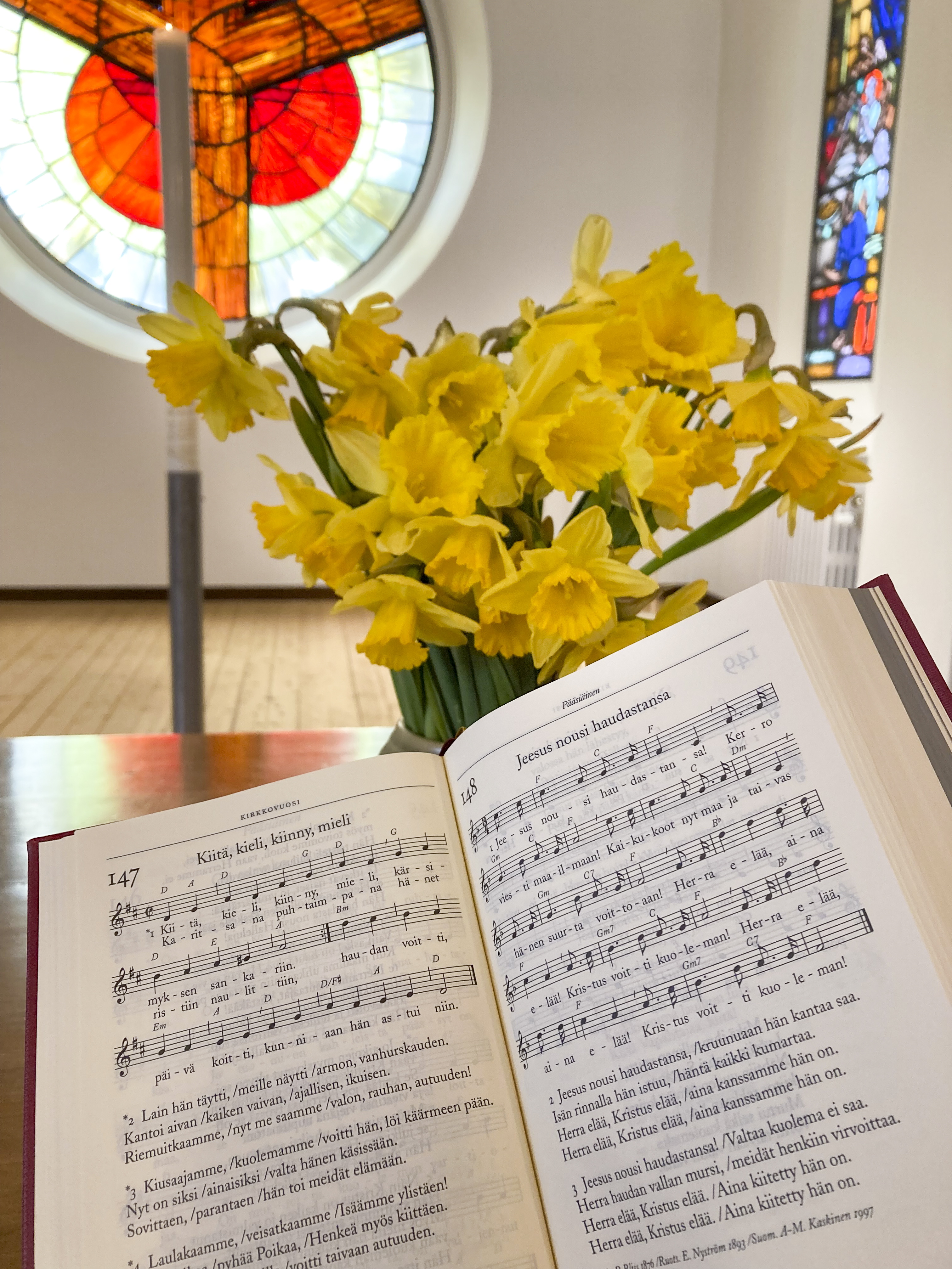 Närbild på en uppslagen finsk psalmbok och påskliljor.