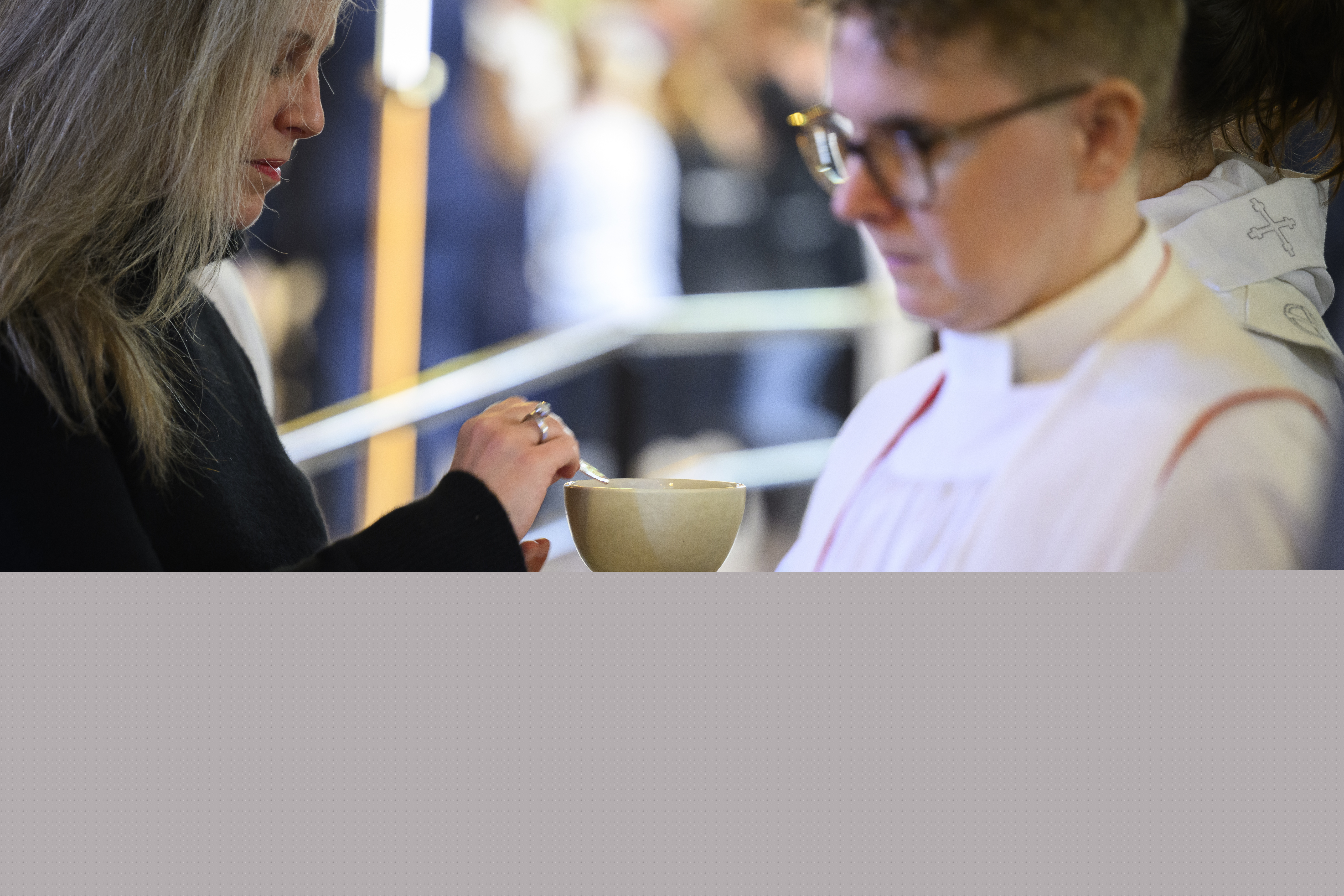 En kvinna i svarta kläder håller en oblat i sin ena hand. Prästen räcker fram kalken.