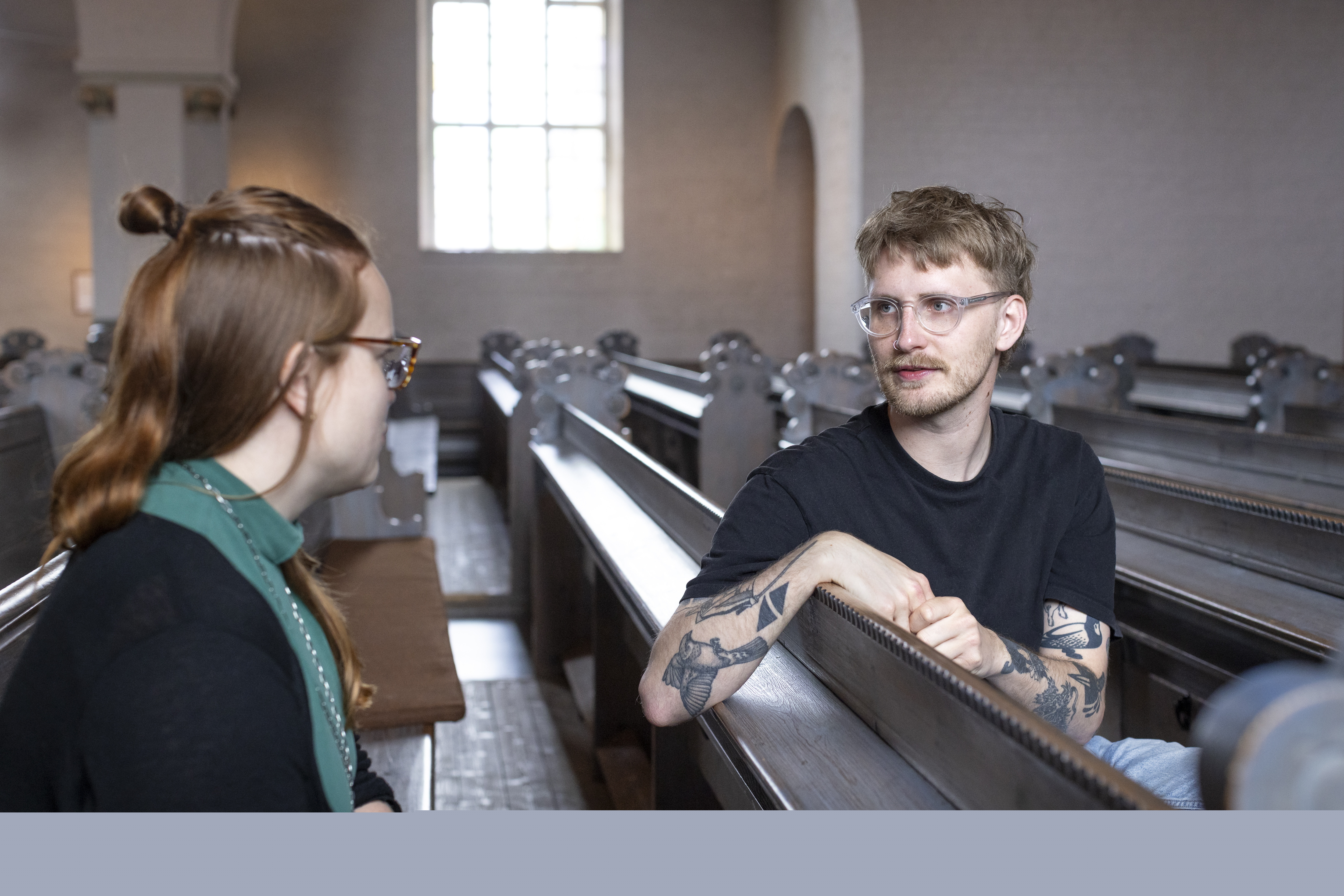 Två personer sitter i en kyrkbänk och pratar med varandra