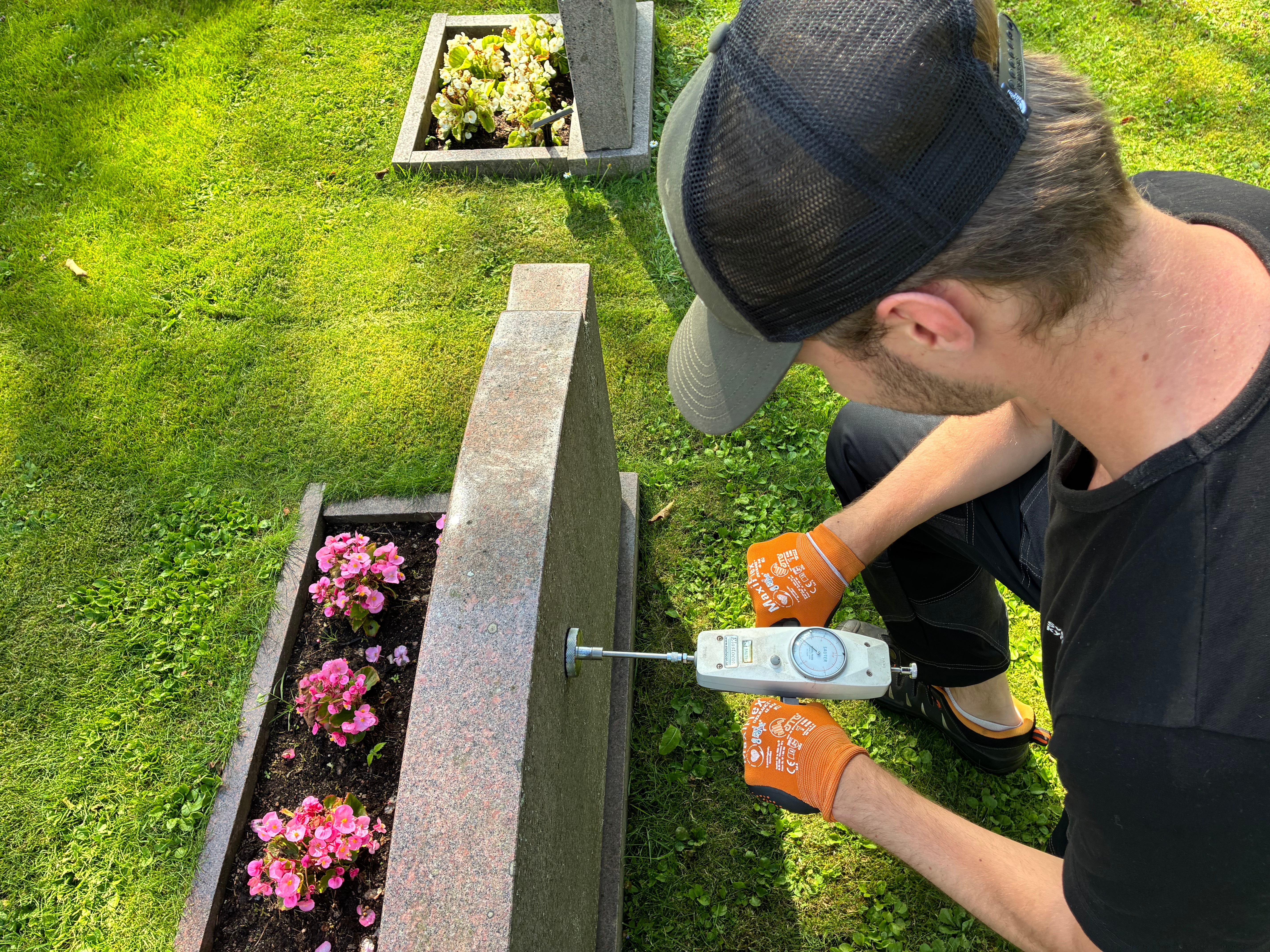 Ett foto av en gravsten som provtrycks. En gravsten måste vara säkert monterad och får inte utgöra en säkerhetsrisk för besökare eller anställda. Vart femte år kontrollerar därför huvudmannen gravstenarna på en gravplats. Stående gravstenar över 30 cm höjd utsätts för 35 kilos tryck och/eller dragkraft vilket de ska klara utan att påverkas. Fotograf Matilda Nyman