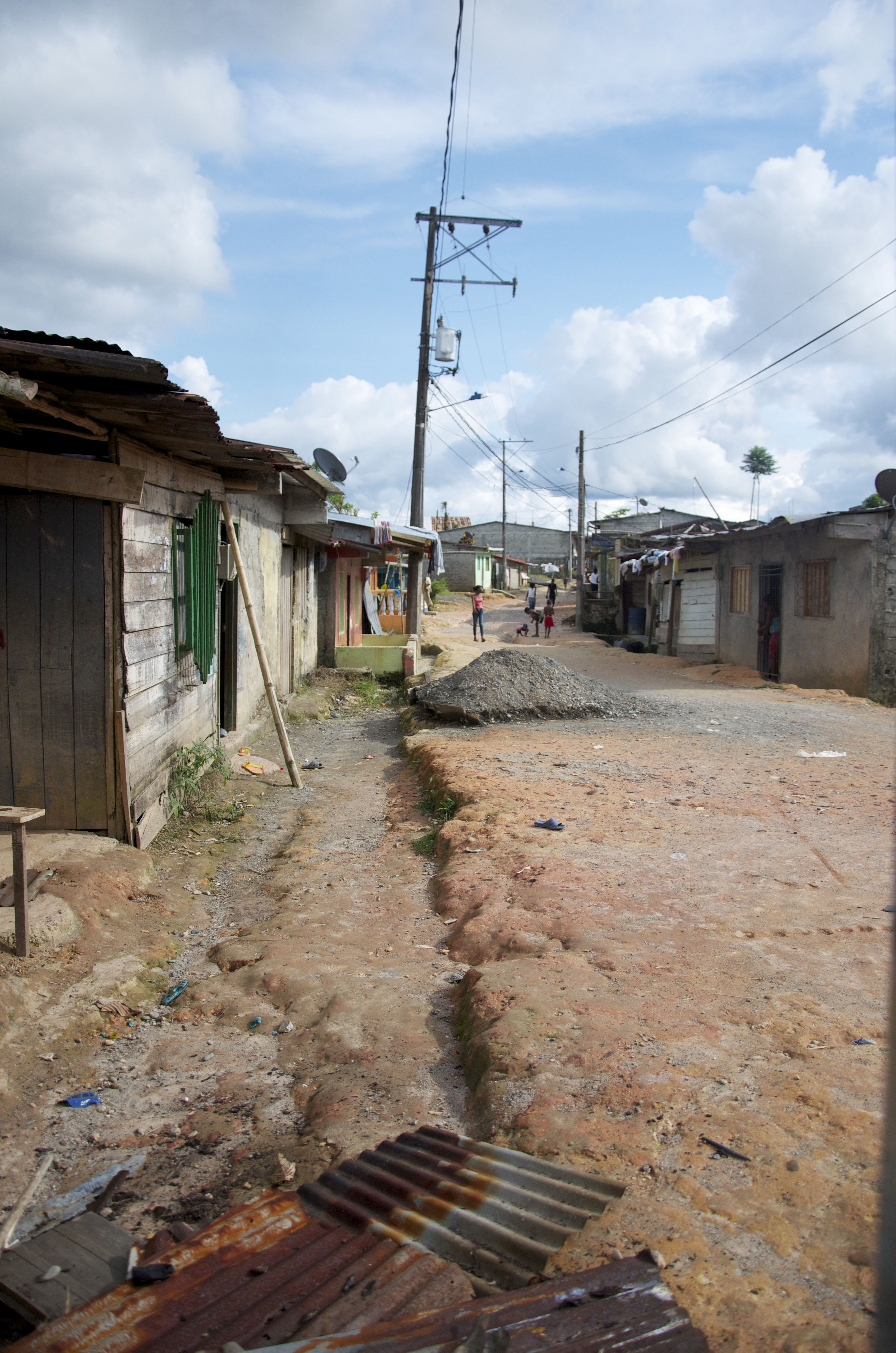 På bilden syns en väg av packad jord som går emellan hus av enkel konstruktion. Längre bort syns några människor. 