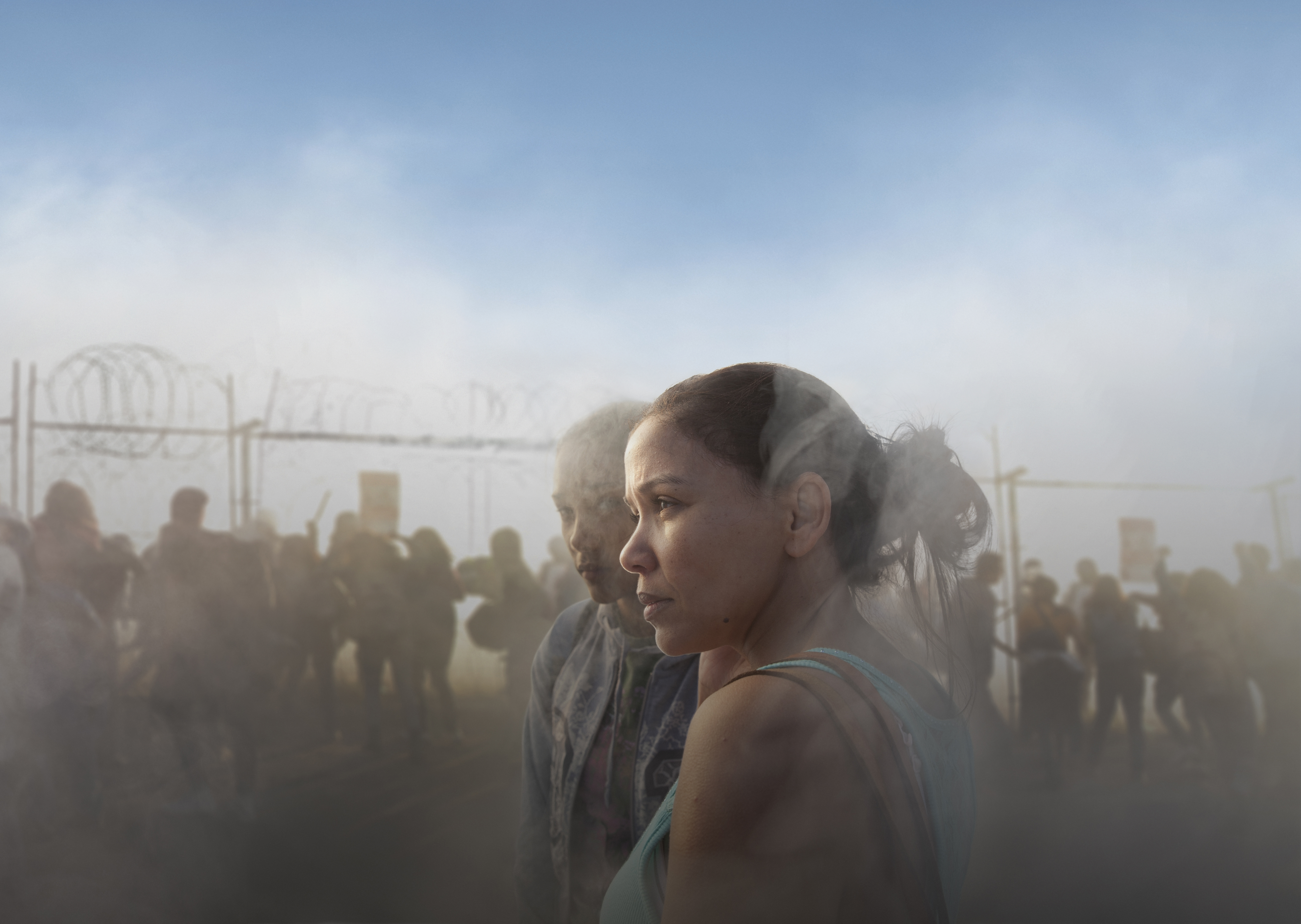 Två kvinnor. Bakom dem syns rök, staket och våldsamma upplopp.