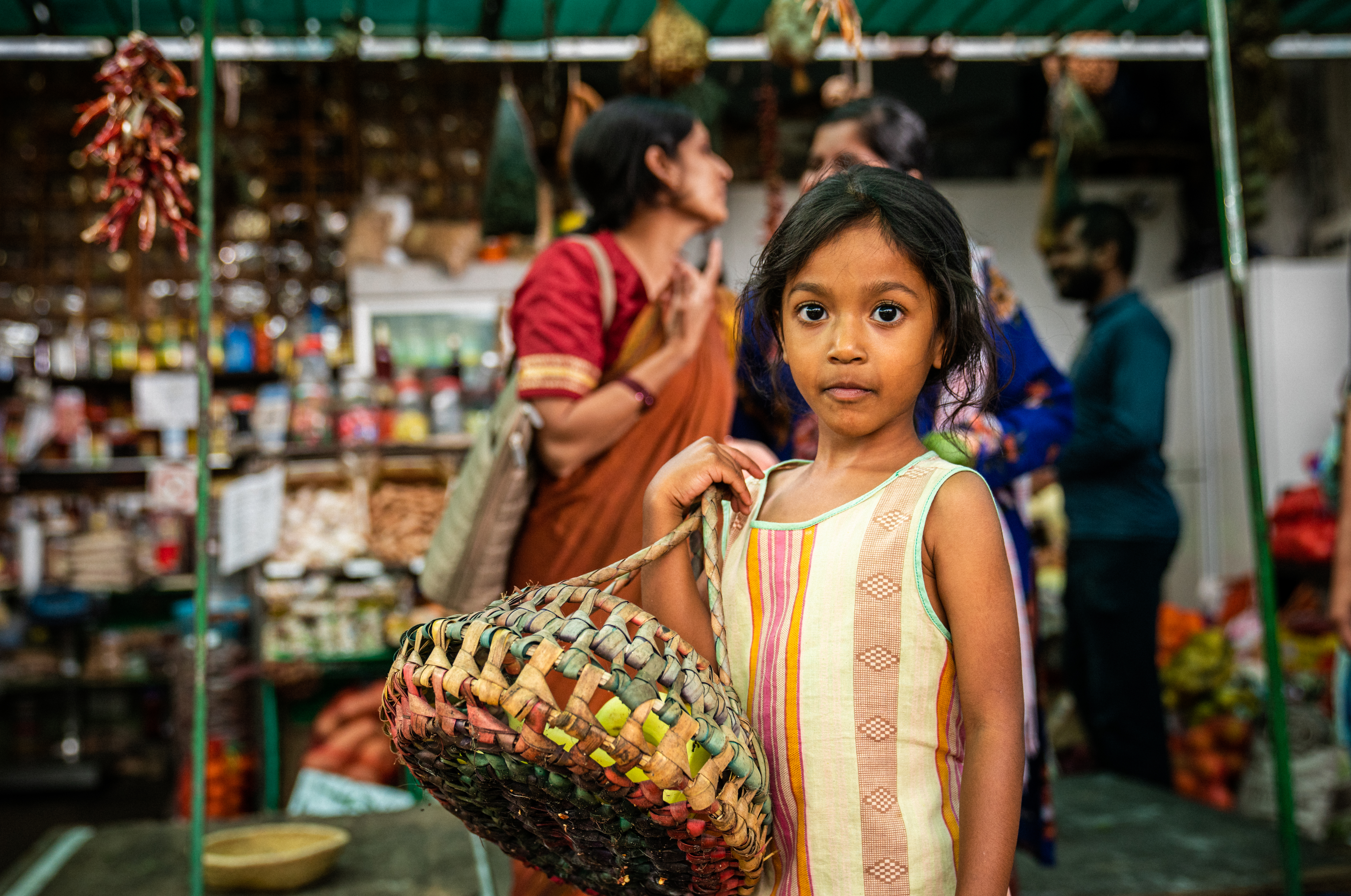 Liten flicka befinner sig på en marknad i Indien. Hon har en flätad korg på sin axel.