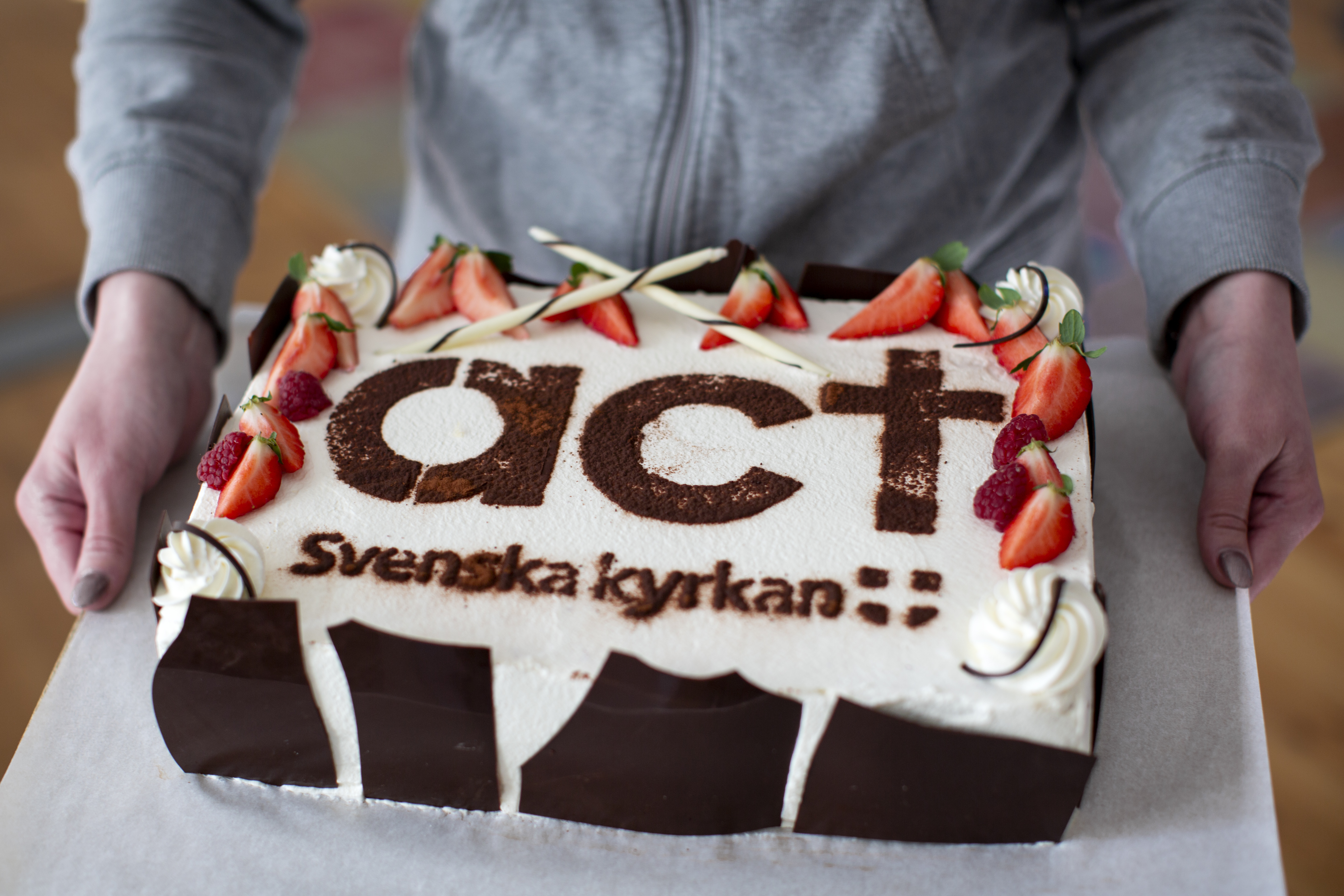 Tåtra med jordgubbar och grädde. På tårtan står det Act Svenska kyrkan.