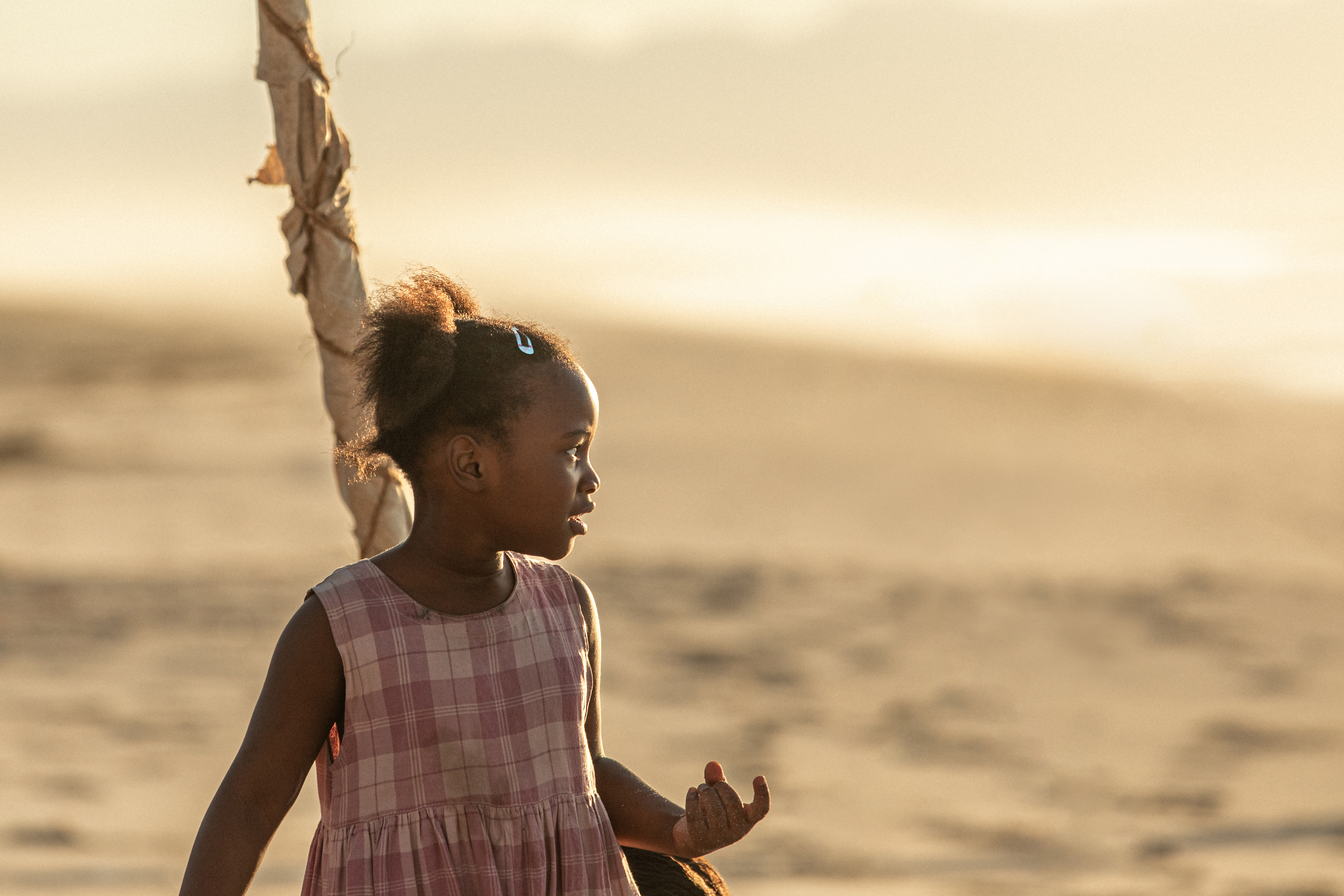 Liten flicka i rosa klänning på en strand i soldengång.