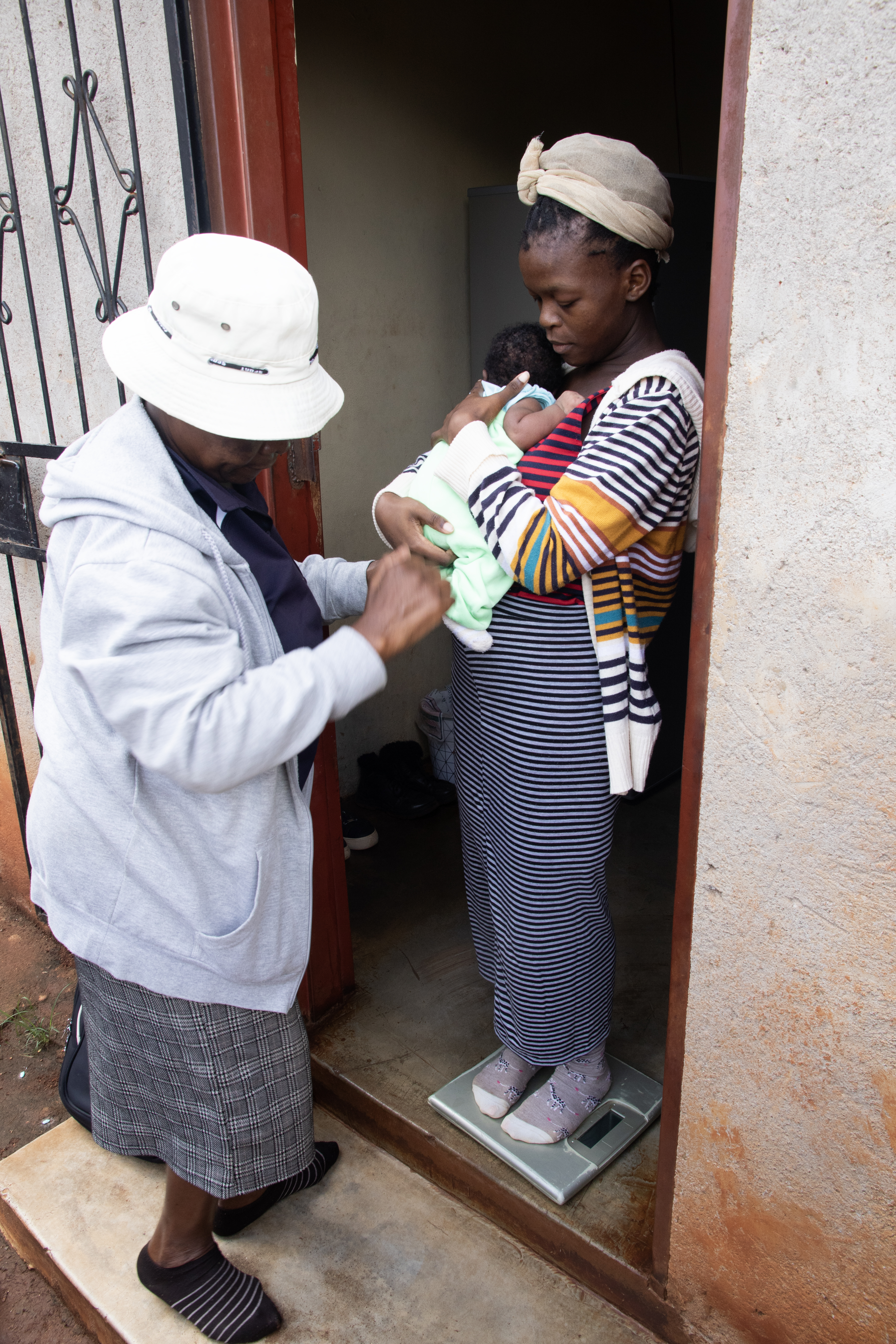 Ung kvinna håller i en liten bebis som undersöks av en mentormamma.