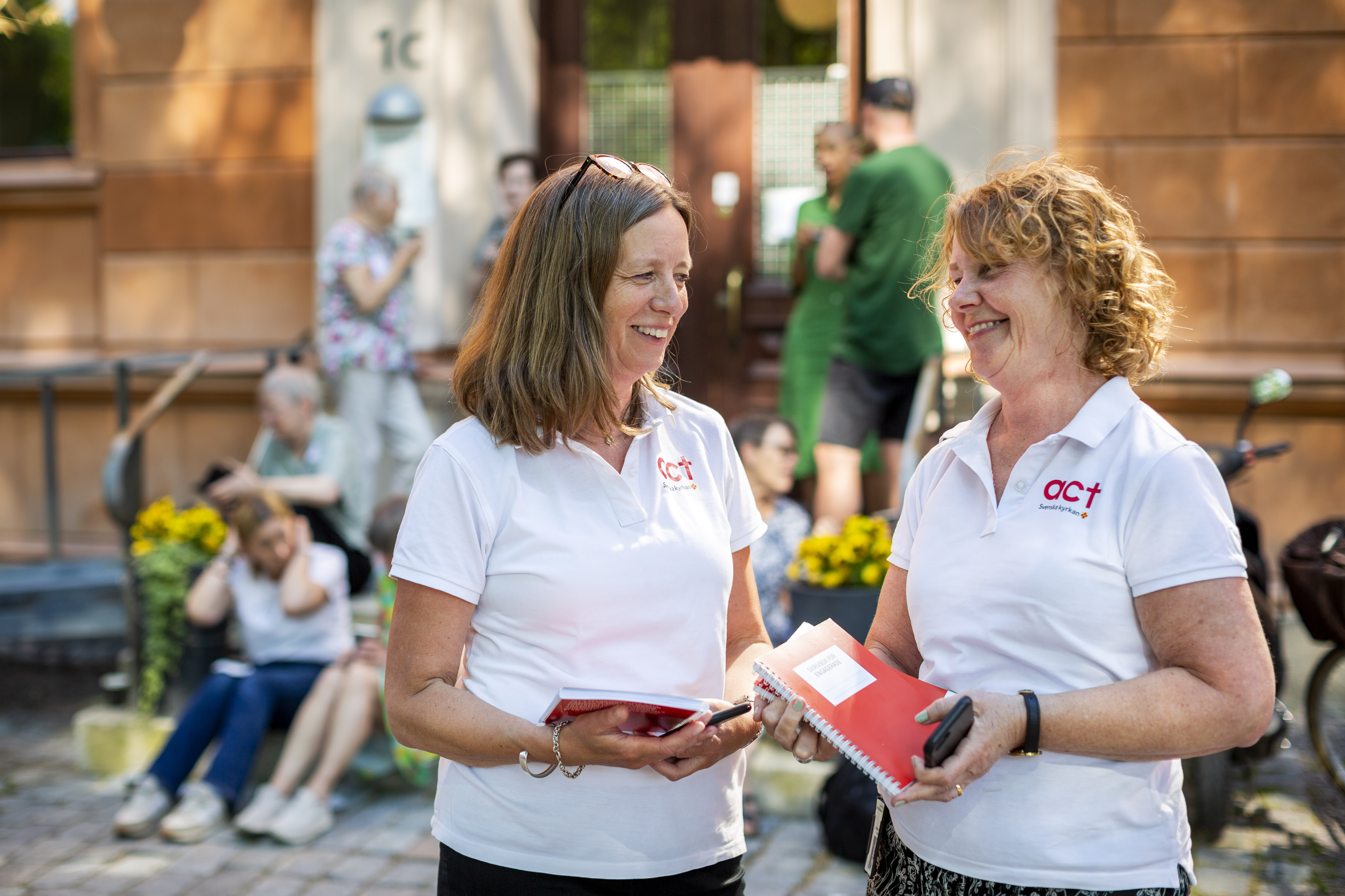 Två kvinnor ler mot varandra. Bakom dem syns fler människor i en trappa.