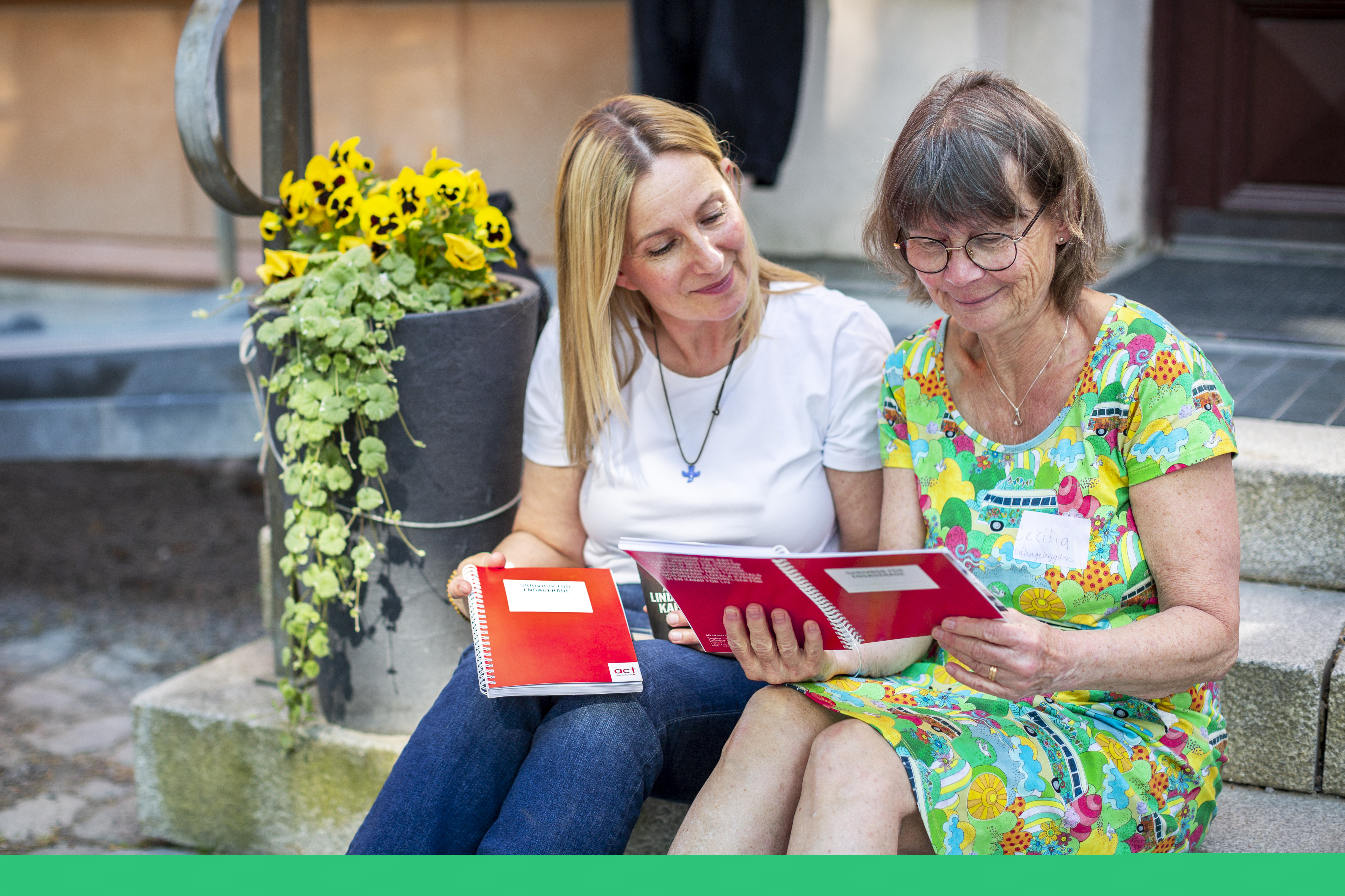 Två kvinnor sitter i en trappa och bläddrar i en bok.