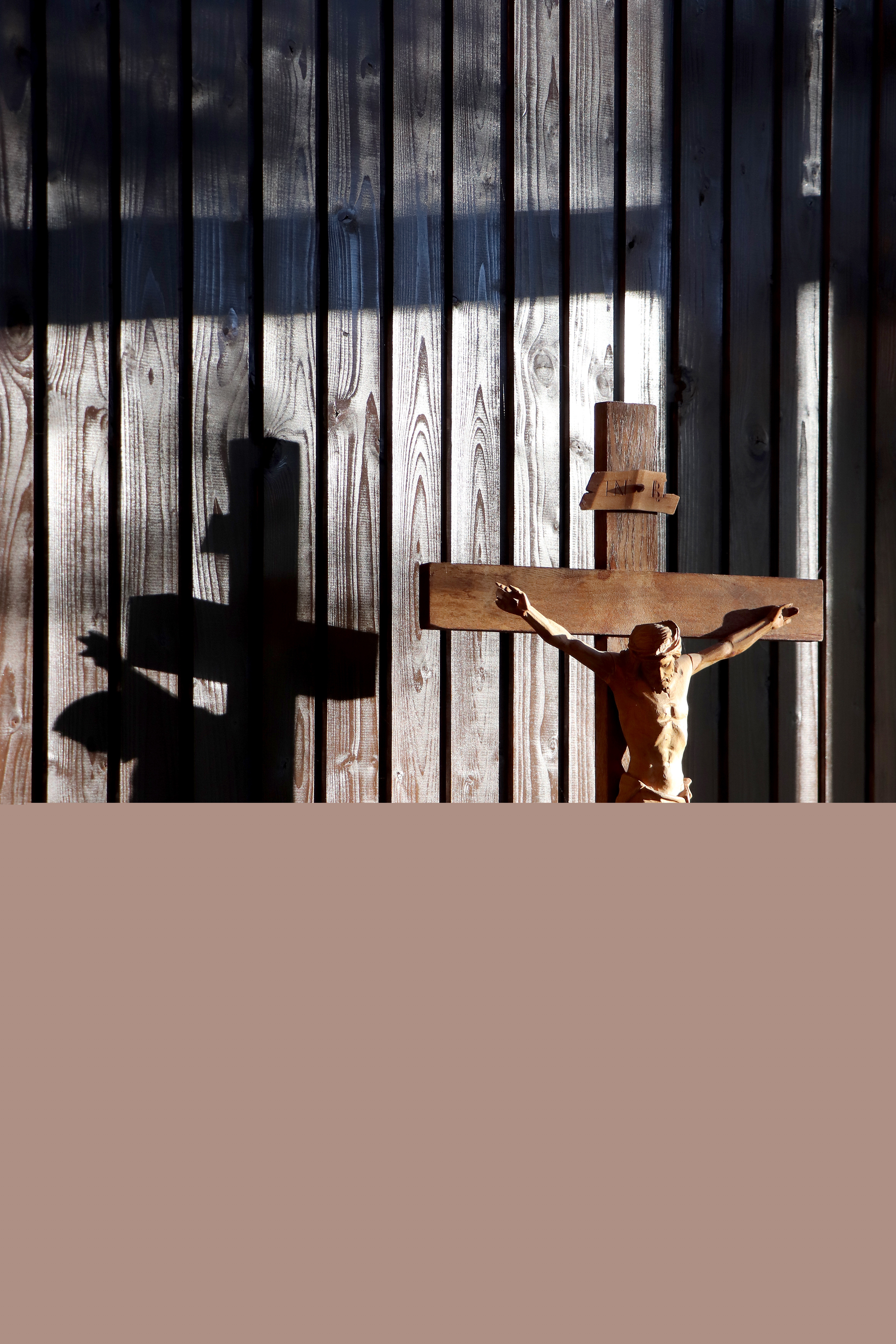 Solen skiner på ett träkrucifix mot träpanel i bakgrunden.