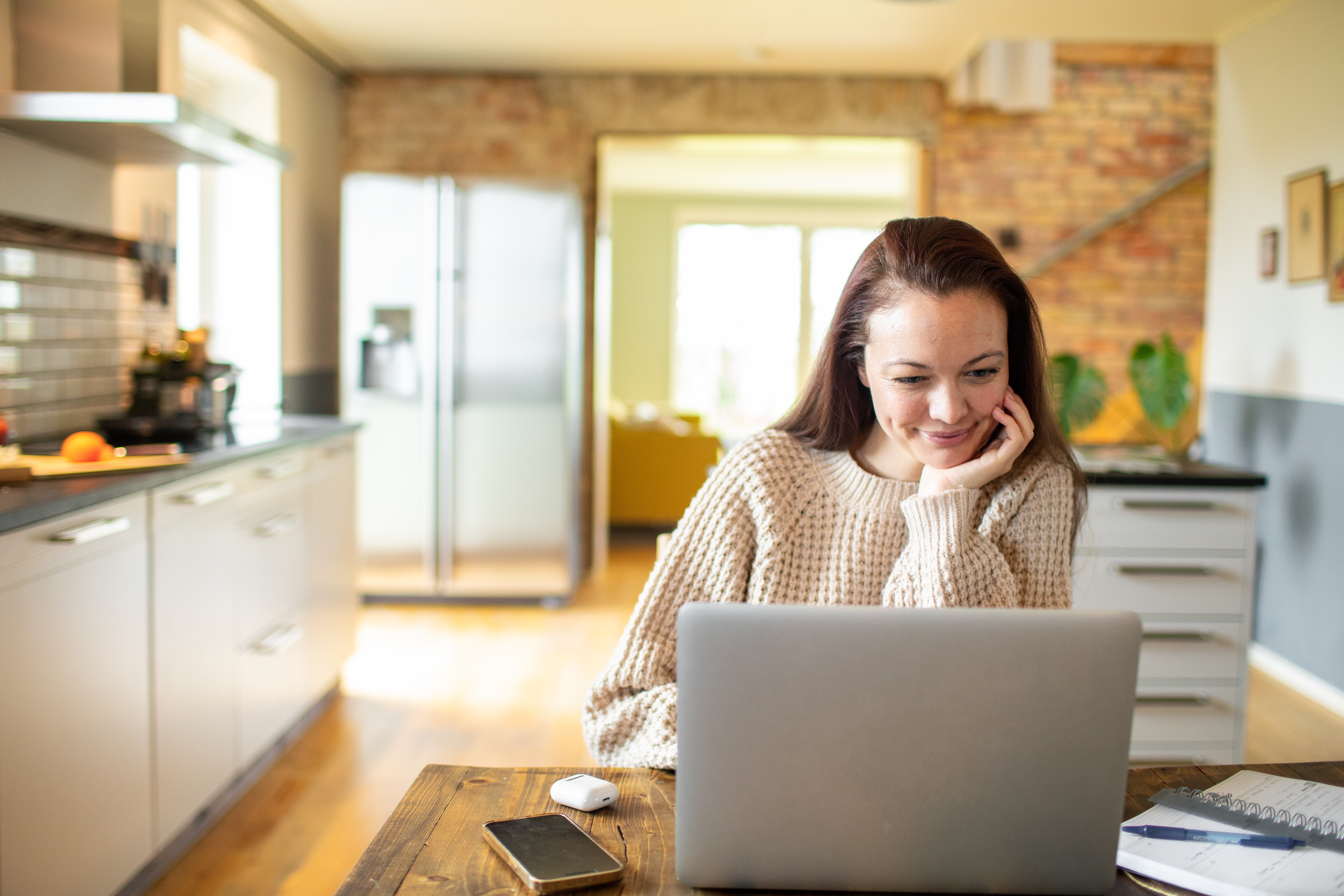 Ung kvinna som använder en bärbar dator i ett kök.