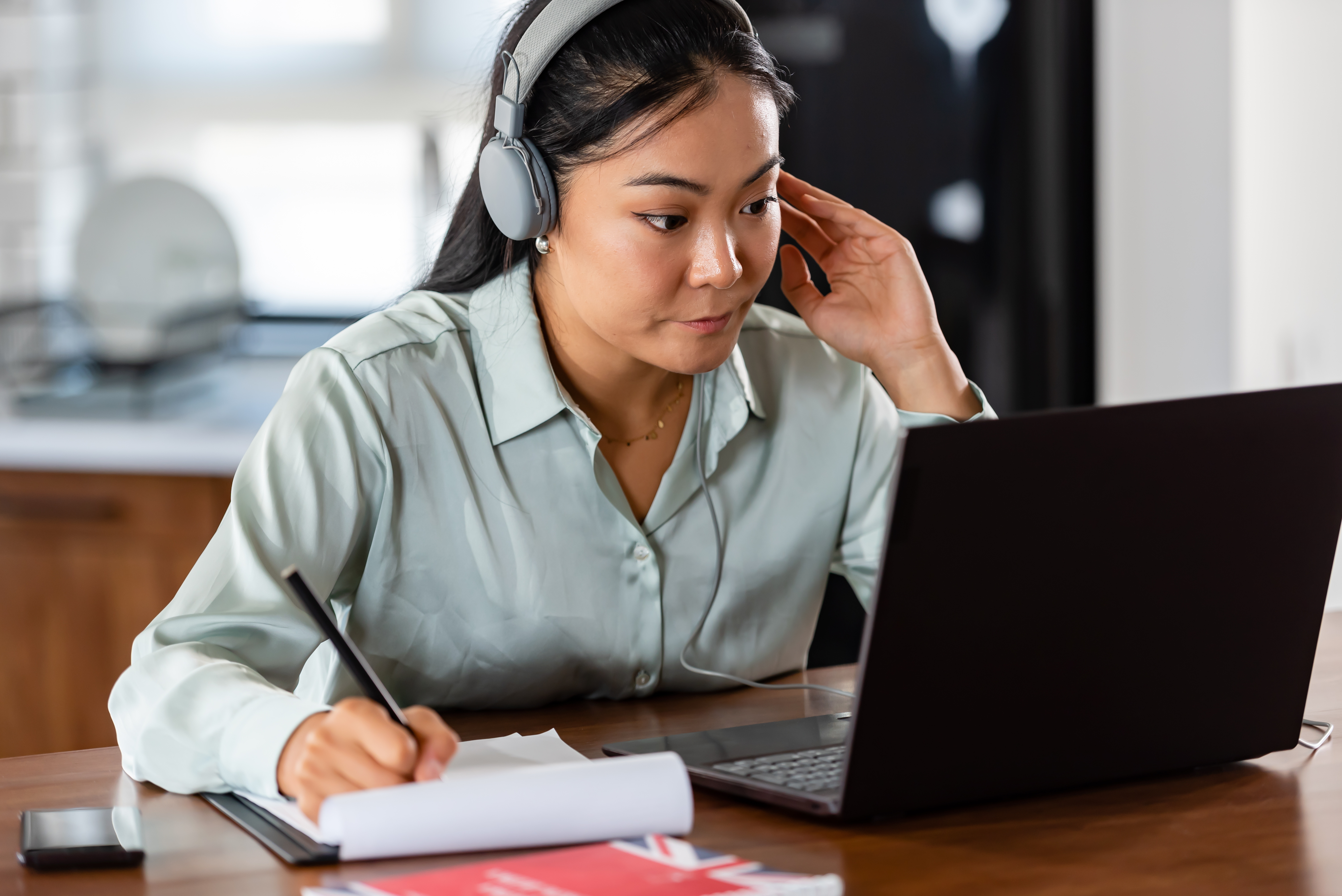 Ung kvinna sitter framför en bärbar dator med hörlurar, lyssnar och antecknar.