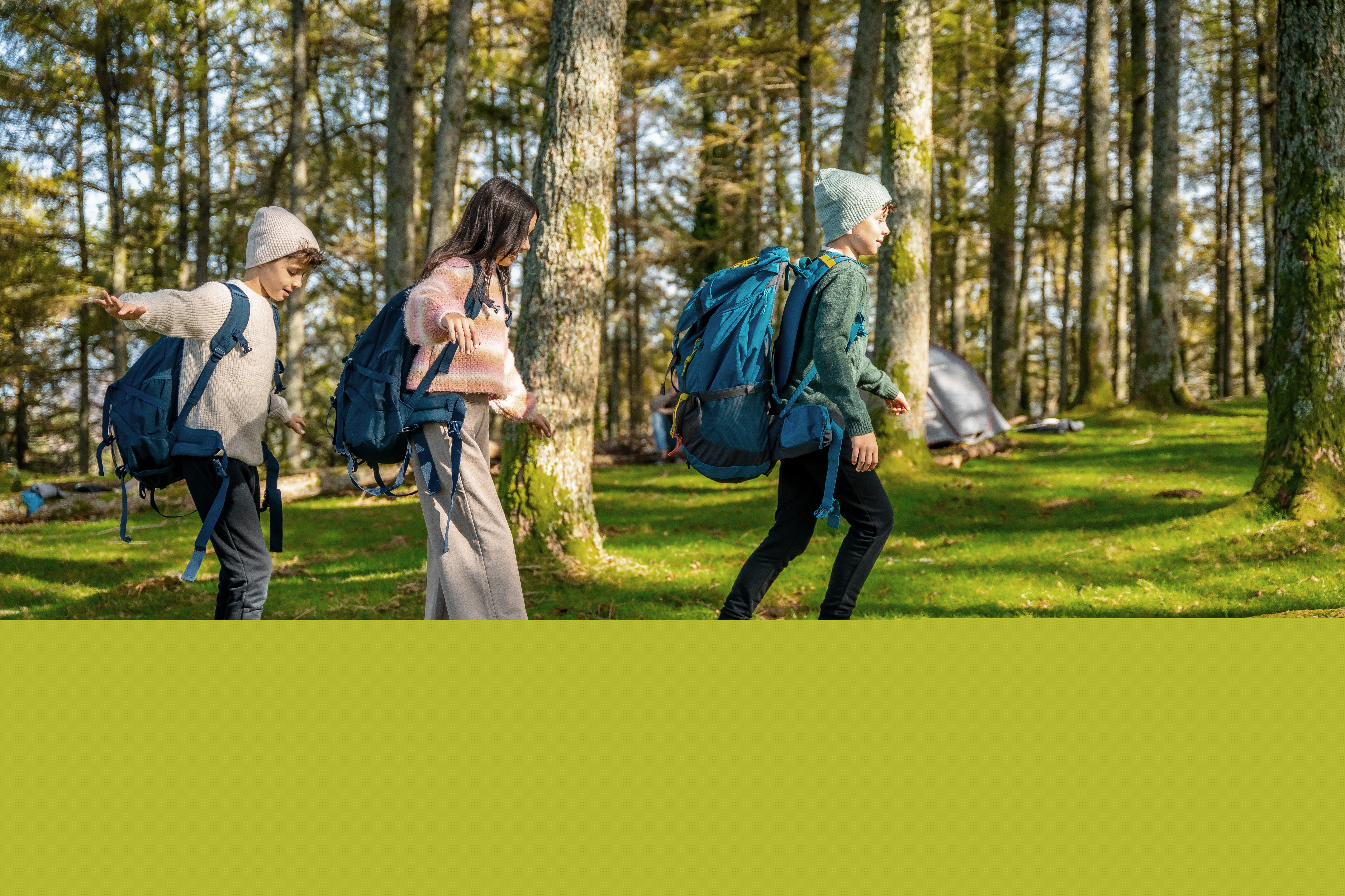 Tre barn balanserar på en fälld trädstam i en grönskande skog.