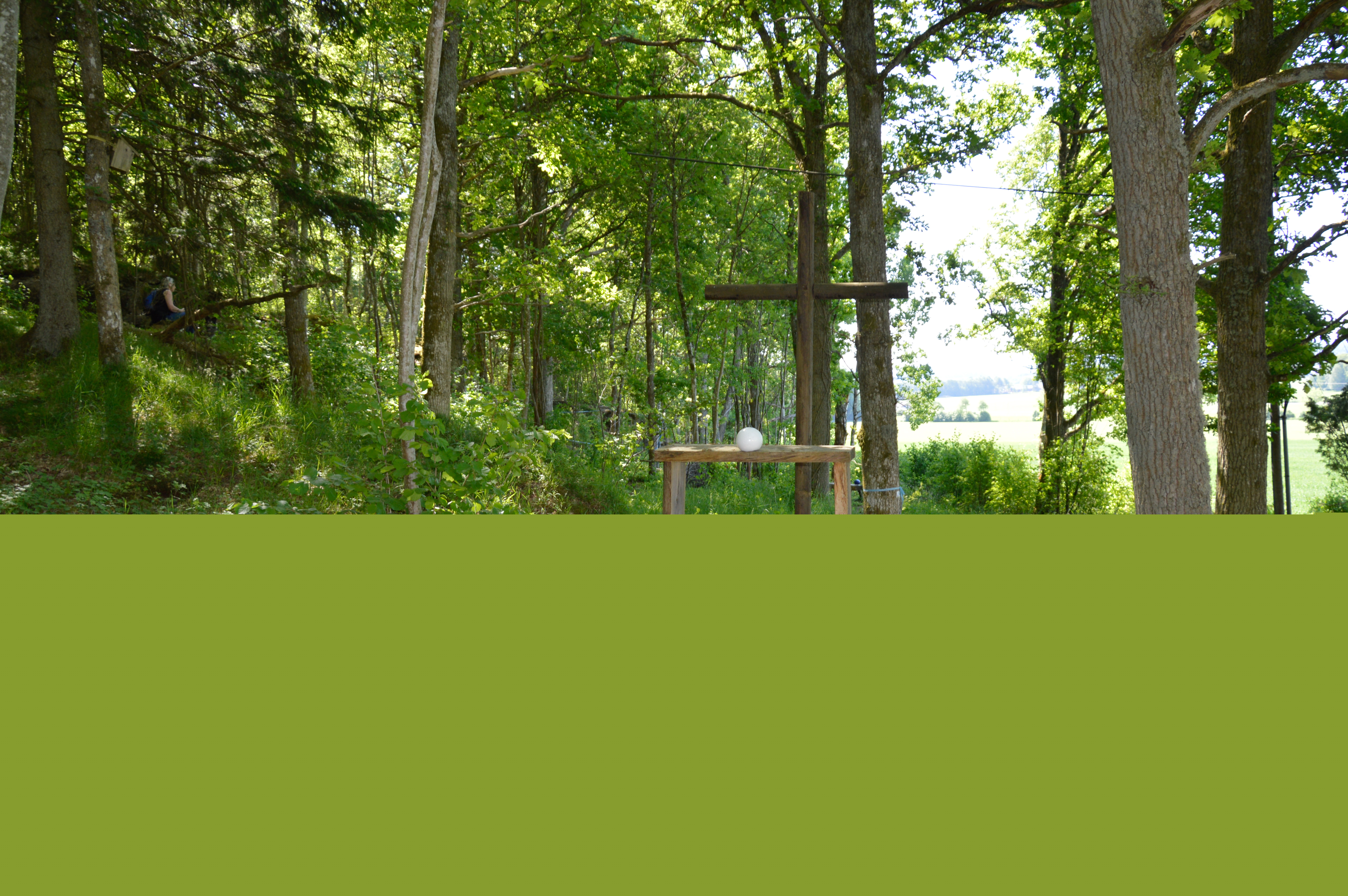 Altare, kors och kyrkbänkar utomhus i en skogsdunge. På altaret ligger en vit stor pärla från frälsarkransvandringen i Östad.