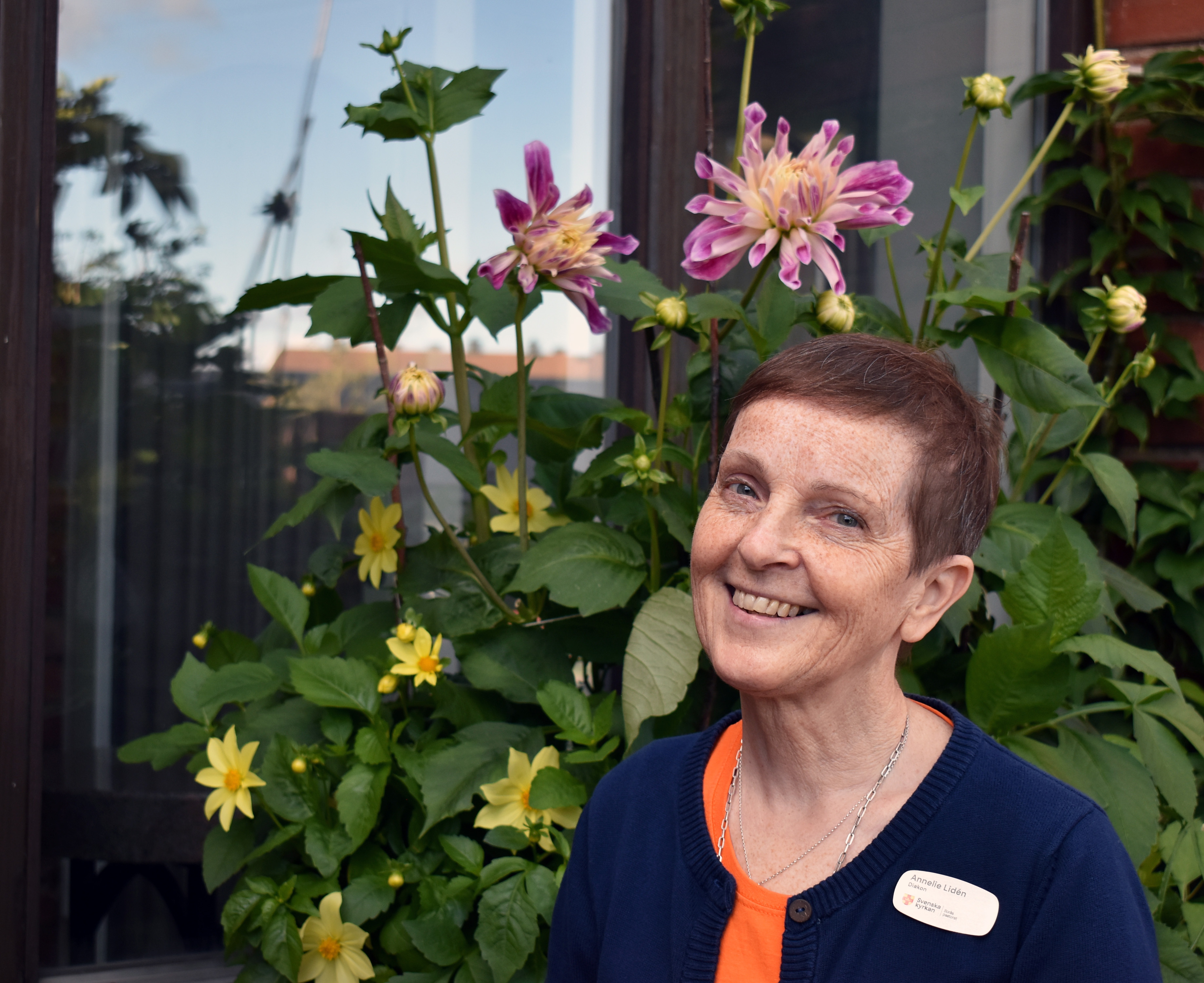 Kvinna omgiven av blommor i rabatt.